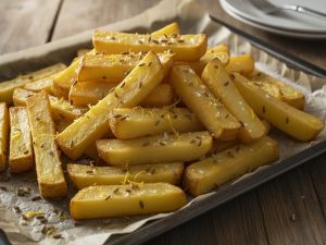 Golden oven-baked french fries on a parchment-lined baking tray, sprinkled with fennel seeds, grated lemon peel and flaky salt