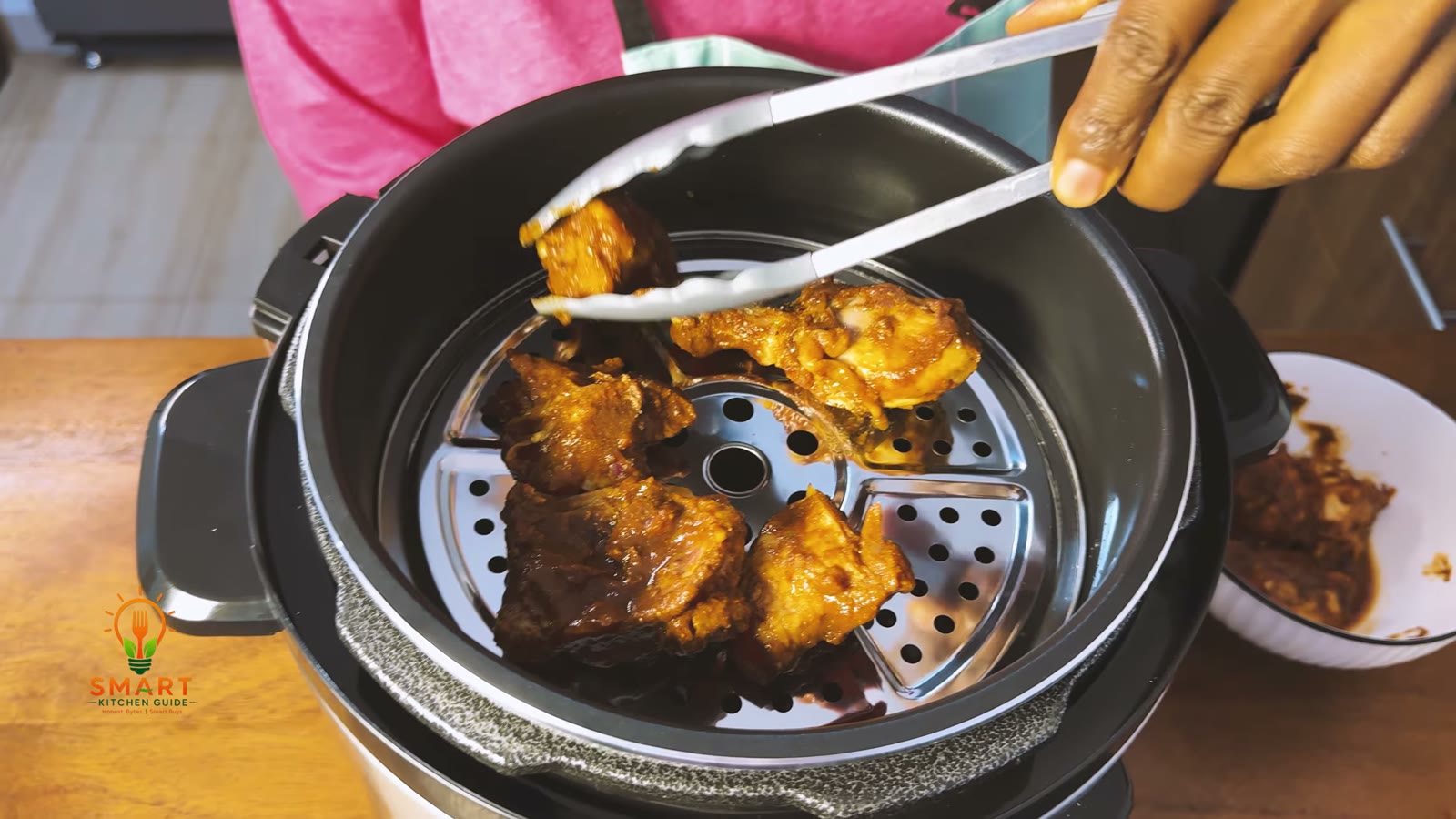 Marinated chicken pieces being placed with tongs on the stainless steam rack inside the Saachi NL-PC-5306