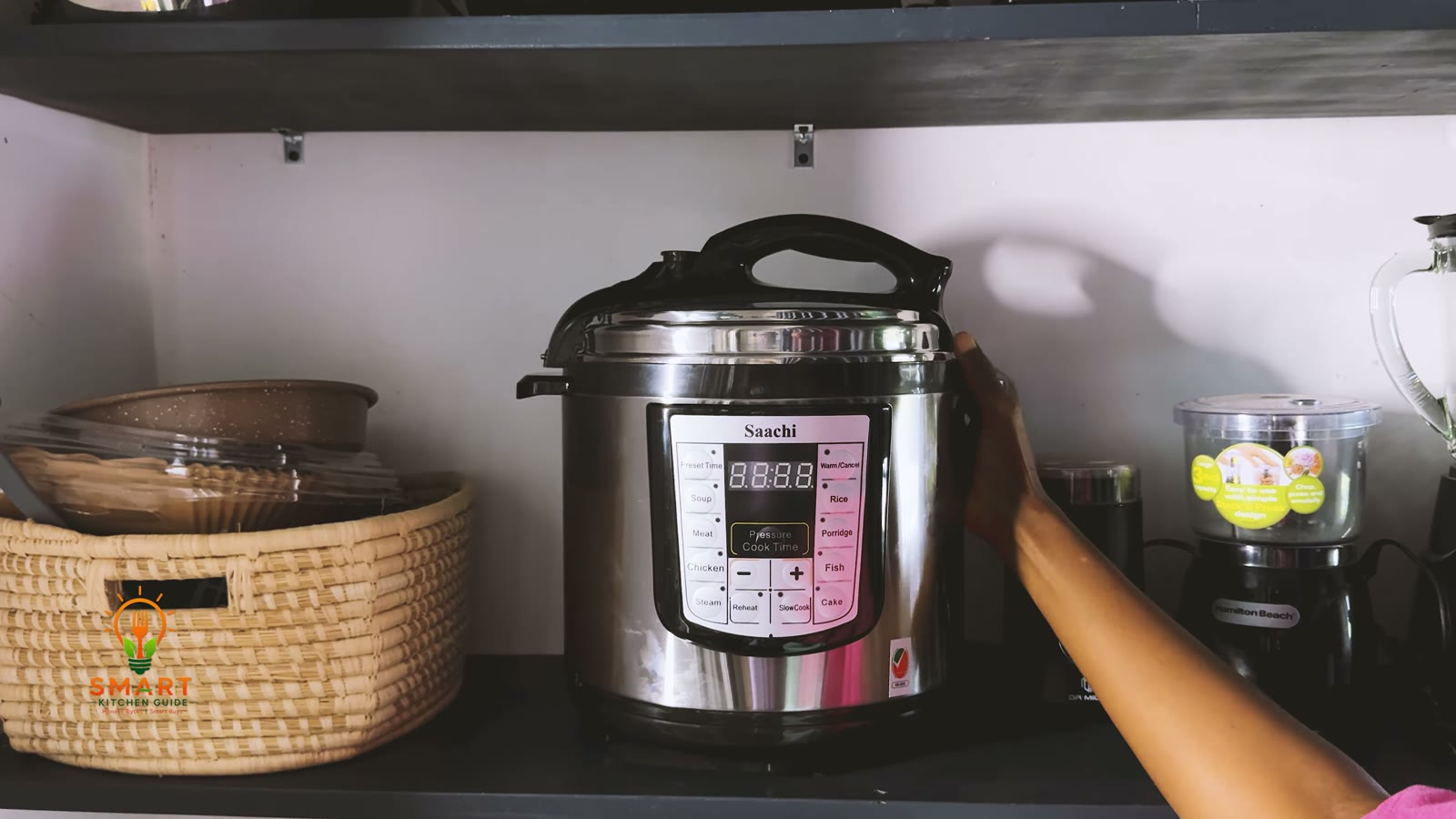 Saachi NL-PC-5306 pressure cooker stored on a kitchen shelf next to a basket and a Hamilton Beach chopper